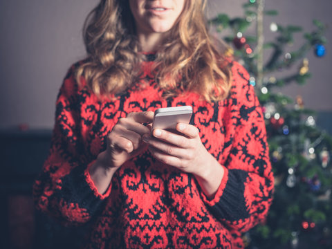 Young woman using smartphone by christmas tree