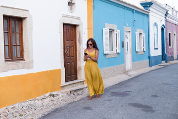 Young woman in yellow dress walking with smart phone on the old streets in the city. Portugal....