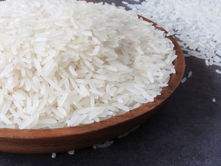 Close up of raw white rice on wooden plate on black background. Rice is the main food of Asians, and the ingredients for traditional Chinese cuisine. Health, nutrition, lifestyle concept. Copy space.