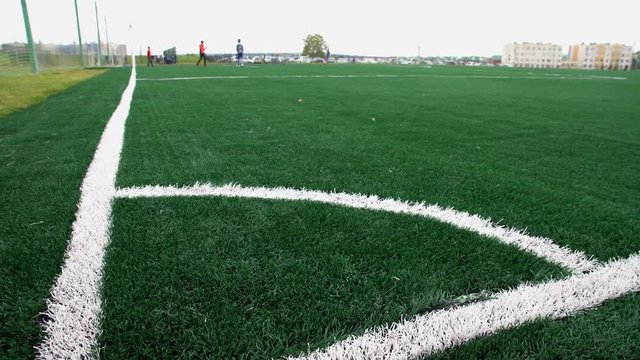 Football field with an artificial lawn. On the background boys play soccer. Focus on foreground