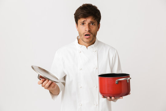 Young chef man standing isolated over white wall background holding crockery.
