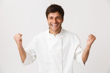 Chef man standing isolated over white wall background looking camera make winner gesture.