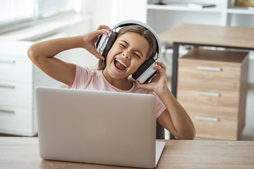 The happy girl in headphones sitting at the desk with a laptop