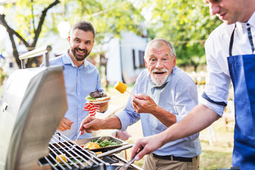 Men with family and friends cooking food on a barbecue party.