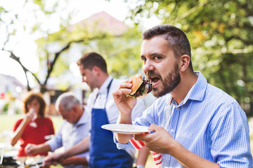 A mature man with family and friends cooking food on a barbecue party.