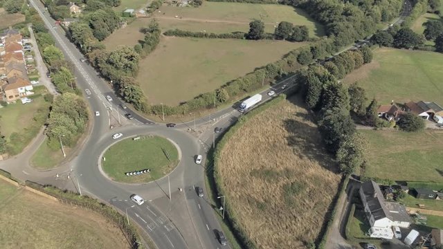 Aerial view, panning move. Traffic on roundabout, houses and fields on Cheshire countryside
