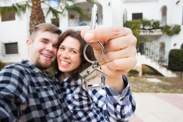 Moving and real estate concept - Happy young laughing cheerful couple man and woman holding their new home keys in front of a house.