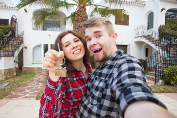 Moving and real estate concept - Happy young laughing cheerful couple man and woman holding their new home keys in front of a house.