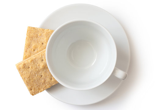 An empty white ceramic cup and saucer with two square shortbread biscuits isolated on white from above.