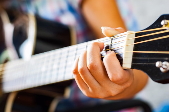 Closeup of young woman hand playing on black acoustic guitar 