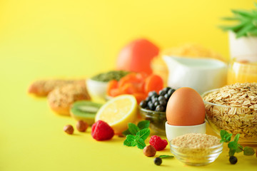 Vegetarian breakfast. Soft boiled egg, oat flakes, nuts, fruits, berries, milk, yogurt, orange, banana, peach on yellow background. Healthy food diet. Copy space. Banner