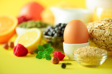 Delicious breakfast ingredients. Soft boiled egg, oat flakes, nuts, fruits, berries, milk, yogurt, orange, banana, peach on yellow background.
