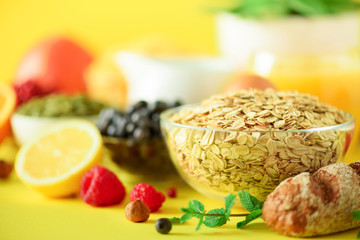 Oat flakes with milk, fresh berries, yogurt, boiled egg, nuts, fruits, orange, banana, peach for breakfast on yellow background. Copy space. Healthy food concept.