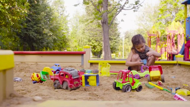 Crane shot. Low angle view. A small girl sitting in a sandbox is picking up something in a mold.