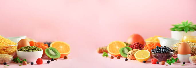 Organic food frame. Banner. Healthy breakfast ingredients. Oat and corn flakes, eggs, nuts, fruits, berries, toast, milk, yogurt, orange, banana, peach on pink background. Top view, copy space