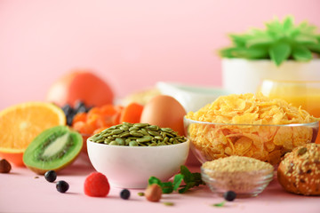 Corn flakes with milk, pumpkin seeds, fresh berries, yogurt, boiled egg, nuts, fruits, orange, banana, peach for breakfast on pink background. Copy space. Healthy food concept.