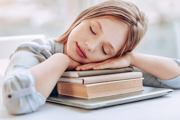 Dreaming about holidays. Pretty blonde girl keeping eyes closed while putting head on books