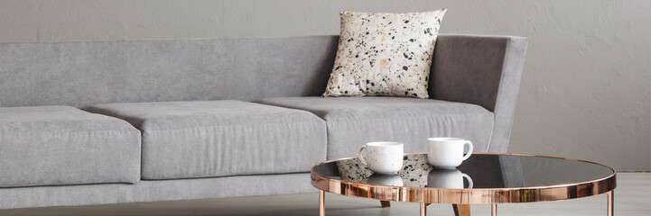 Real photo with close-up of two coffee cups placed on rose gold end table in room interior with grey sofa with lastrico cushion - obrazy, fototapety, plakaty