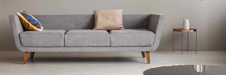 Grey lounge with two pillows standing in bright living room interior with rose gold end table with jug in the real photo
