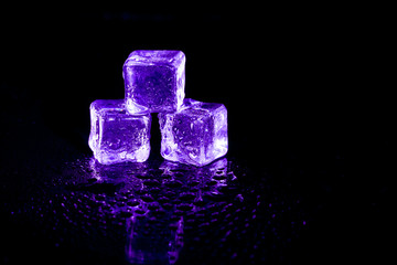 Purple ice cubes reflection on black table background.
