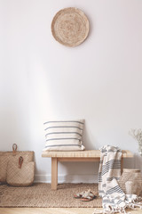 Pillow and blanket on wooden stool in white living room interior with brown plate. Real photo
