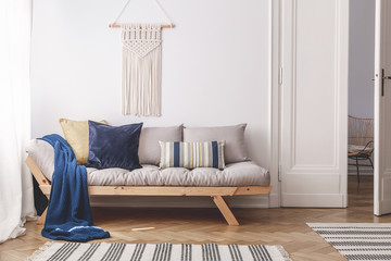Blue blanket and pillows on grey wooden couch in white living room interior with door. Real photo