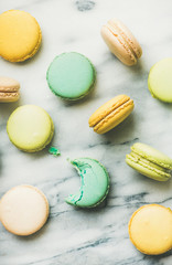 Flat-lay of sweet colorful French macaroon cookies over grey marble background, top view, vertical composition