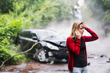 A young woman with smartphone by the damaged car after a car accident, making a phone call. - Powered by Adobe