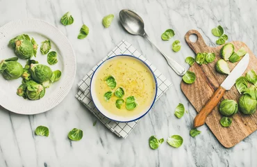 Foto op Aluminium Flat-lay of seasonal brussels sprouts vegetable cream soup in bowl and fresh green brussel sprouts over marble background, top view. Vegan, vegetarian, healthy, dieting food concept © sonyakamoz