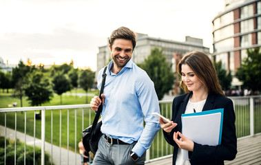 A young businessman and businesswoman walking on a bridge, using smartphone.