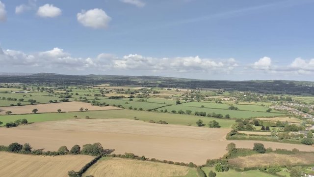 Aerial view, panning move. Fly over Cheshire fields, small town, Tarvin on a sunny day