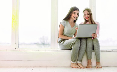 Missing you. Beautiful females feeling happiness while sitting together on windowsill