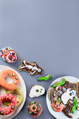 Halloween sweet treats, party food concept. Scary cookies, monster biscuits and fruits on grey background.