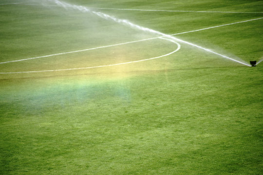 Regenbogen unterm Rasensprenger / Die grüne Rasenfläche eines Fußballfeldes mit einer Bewässerungsanlage die einen Regenbogen erzeugt...