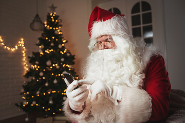 Santa Claus using a phone, sitting in a cozy room 
