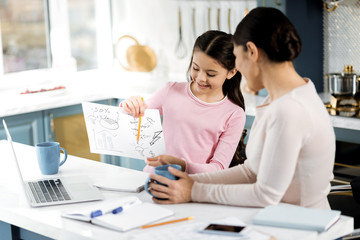 Team work. Serious glad girl demonstrating picture and woman holding cup