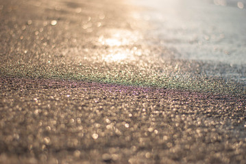 Sandy beach in the rays of sunset and surf, blurred background with the effect of dispersion from lenses