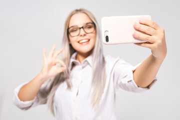 Portrait of a smiling cute woman in glasses making selfie photo on smartphone isolated on a white background.