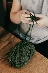 Young girl sitting at the wooden table and learning knitting with green yarn. Relaxing hobby, learning concentration.