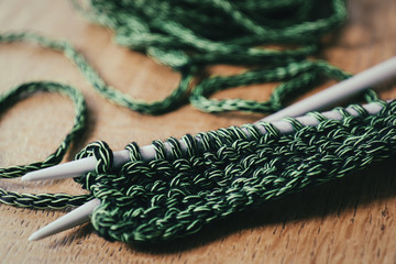 Green yarn with knitting needles and some knitted rows. Relaxing hobby.