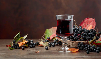 Fresh juice of ripe black chokeberry in glass and berries with leaves.