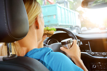 Woman as a driver eats and drinks during the car ride and is therefore careless and distracted