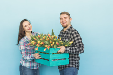 Happy man and woman florists holding box with tulips and laughing on blue background
