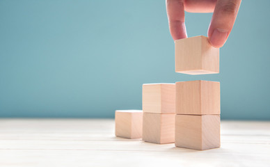 Hand arranging wood cube stacking as step stair. Business concept growth success process on blue background, copy space.