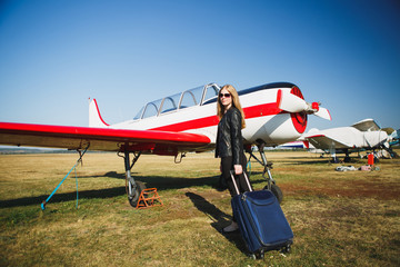 Beautiful woman in black leather jacket standing in front of small vintage aircraft