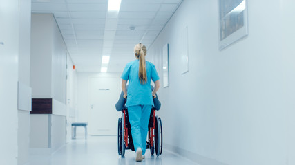 Shot of the Female Nurse Moving Patient in the Wheelchair Through the Hospital Corridor. Doing...
