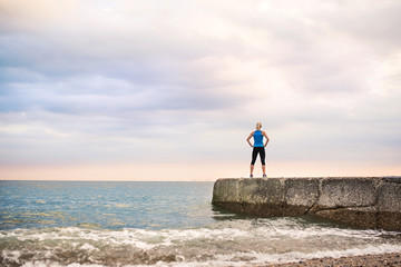 Rear view of young sporty woman standing on a pier by the ocean outside.