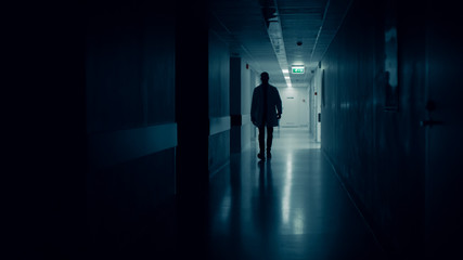 Fototapeta na wymiar Medical Doctor Silhouette Walks in Dark Part of the Hospital Corridor.