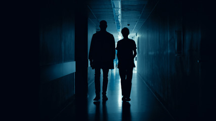 Fototapeta premium Medical Staff Silhouettes Walk in Dark Part of the Hospital Corridor.