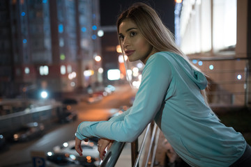 Woman silently standing on the terrace and thinking, night city background